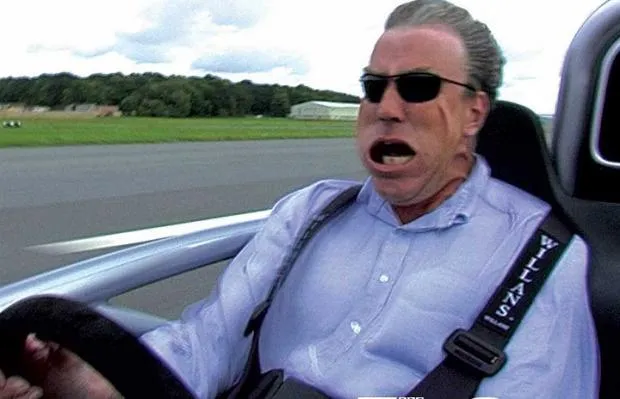 Man in sunglasses gripping a car seat with his face distorted by g-force while riding in a high-speed car on a track